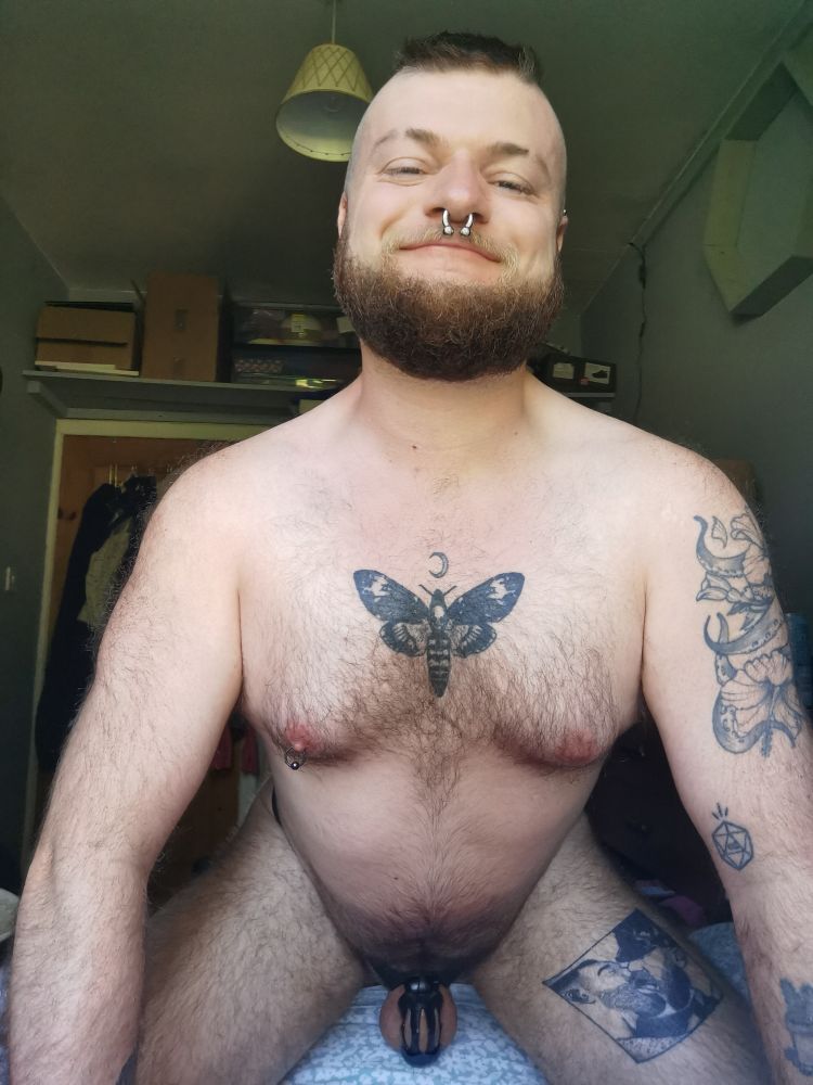 Photo of me on all fours naked on a bed, my chastity cage hanging low and ive got a warm grin on my face