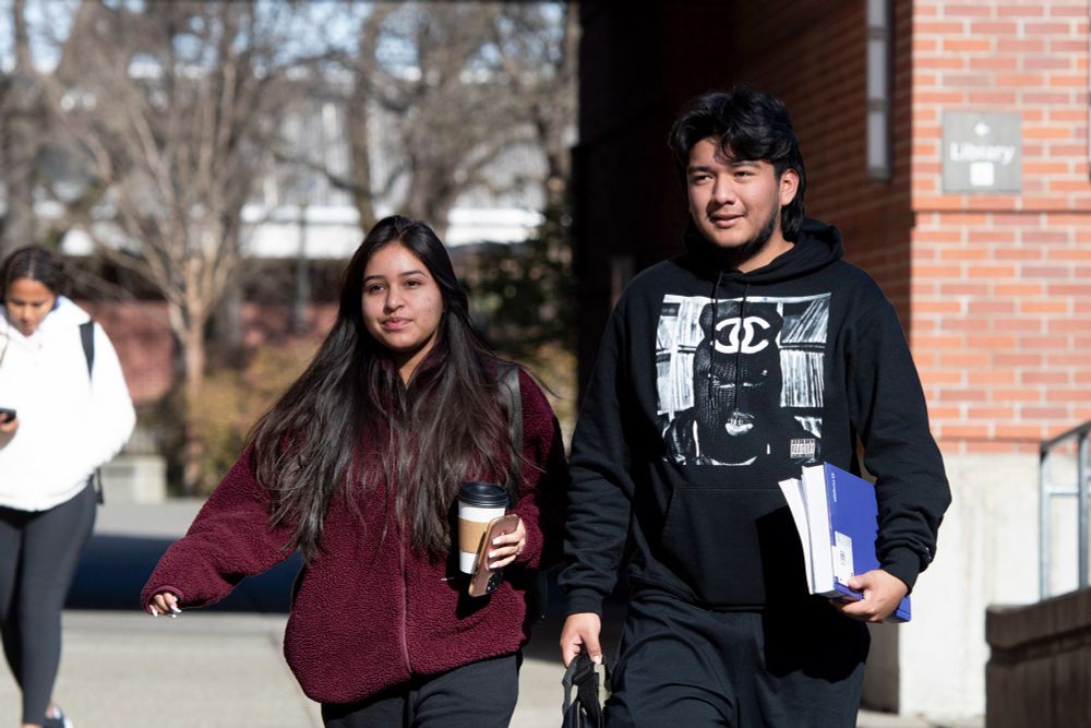 A female and a male student are walking on the Santa Rosa Junior College's campus, holding notebooks and coffee. 