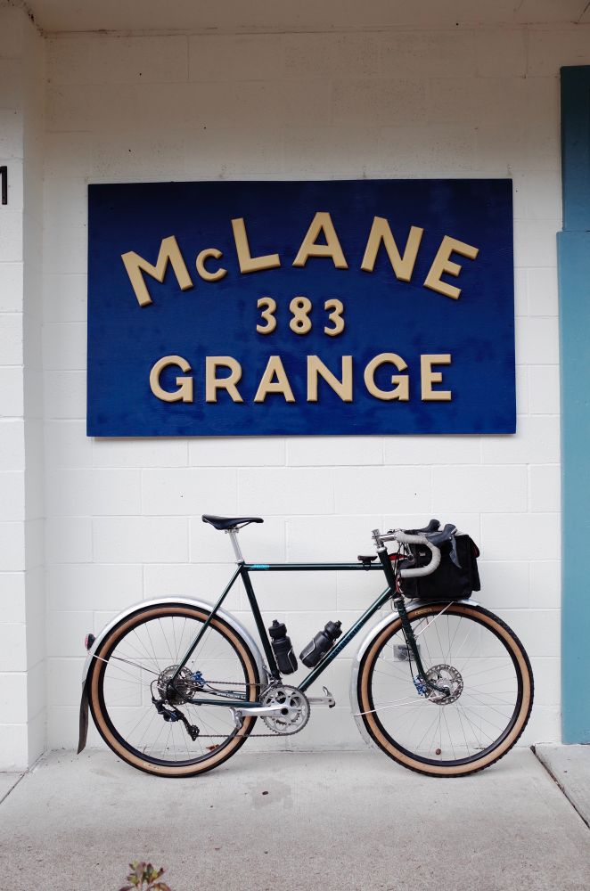 Green bicycle leaning against a white wall with a blue sign that says McLane Grange