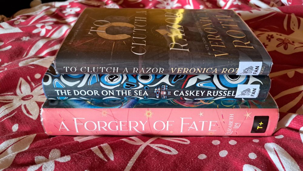 A stack of hardback library books: To Clutch a Razor by Veronica Roth, The Door on the Sea by Caskey Russell, A Forgery of Fate by Elizabeth Lim 