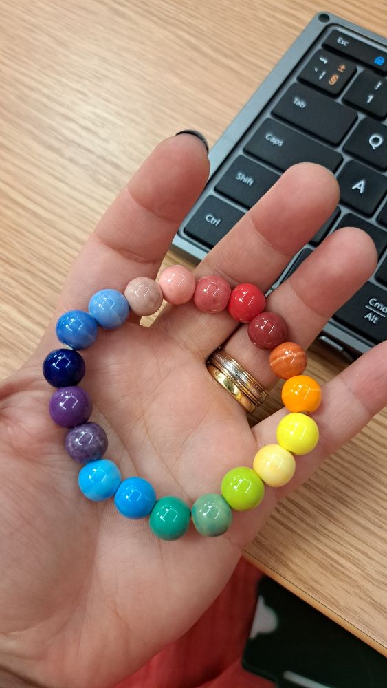A bracelet made of chunky spherical ceramic beads in consecutive shades of colours, like a colour wheel 