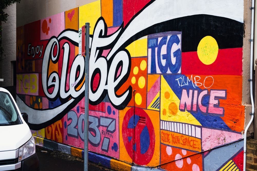A photo of graffiti on a wall in the Sydney Australia district of The Glebe. The name of Glebe is in the style of the Coke logo and says "Enjoy Glebe".