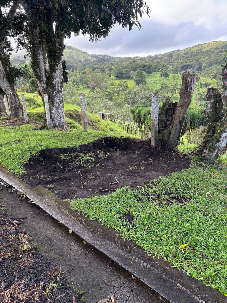 Dirt circle in the middle of a grassy stretch, in front of green rolling hills covered in trees