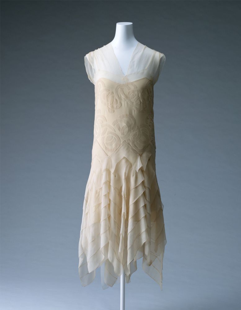 Sleeveless dress in ivory silk chiffon; with appliqué of circle motif; and a bias-cut skirt with seven layers of the same fabric.