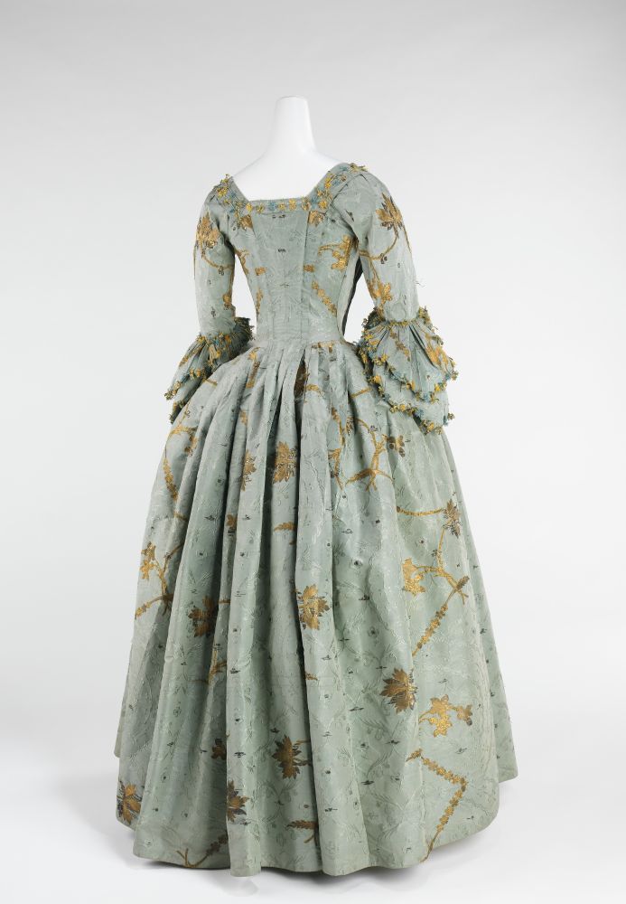 Image 2
Rear view of the dress from image 1. The skirt is pleated at the back, with a continuation of the gold detailing. In this image you can also see the structure of the skirt more clearly, with large panniers given the hips more form, and a snugly fitted bodice. 