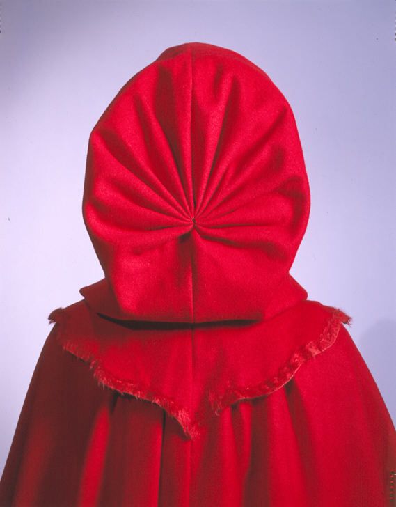 Image 2. Rear view of the cape from image 1, showing a close up of the back of the hood and collar. The material of the hood is gathered to a point at the base of the skull. The collar tapers to a point at the spine, and has a rough cut edge. 