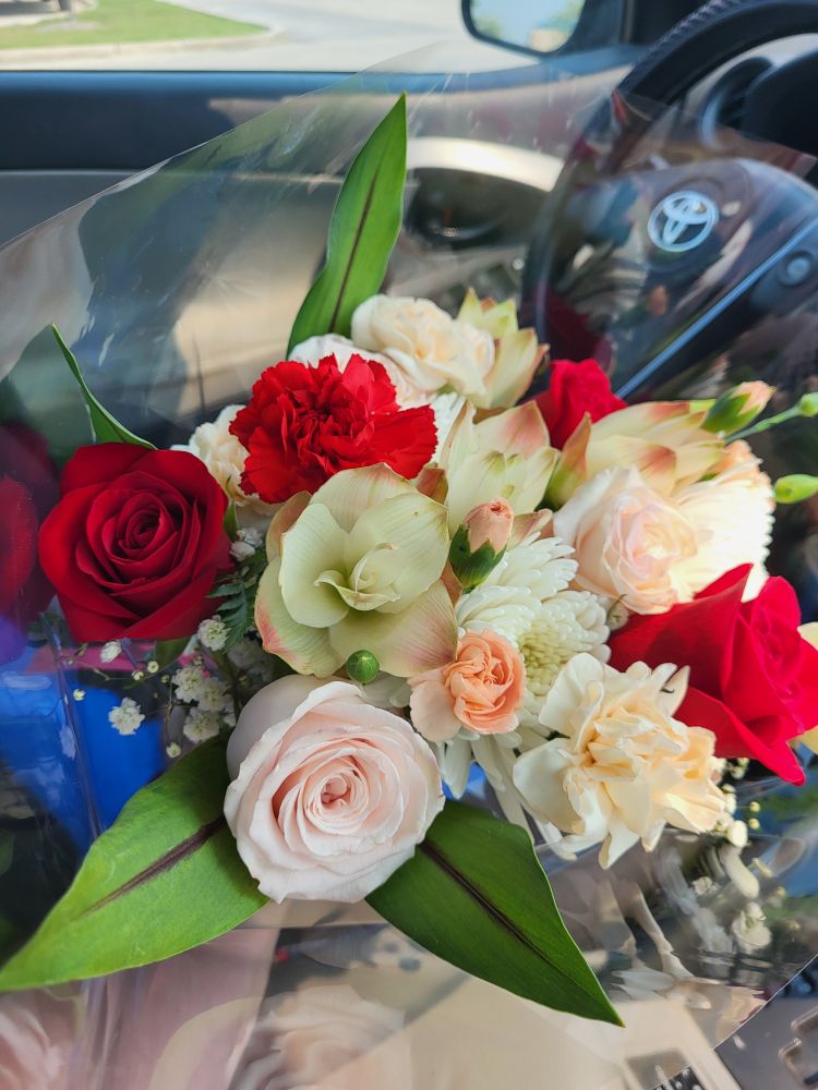 A bouquet of flowers held towards the camera. The picture also has the interior of a car.
