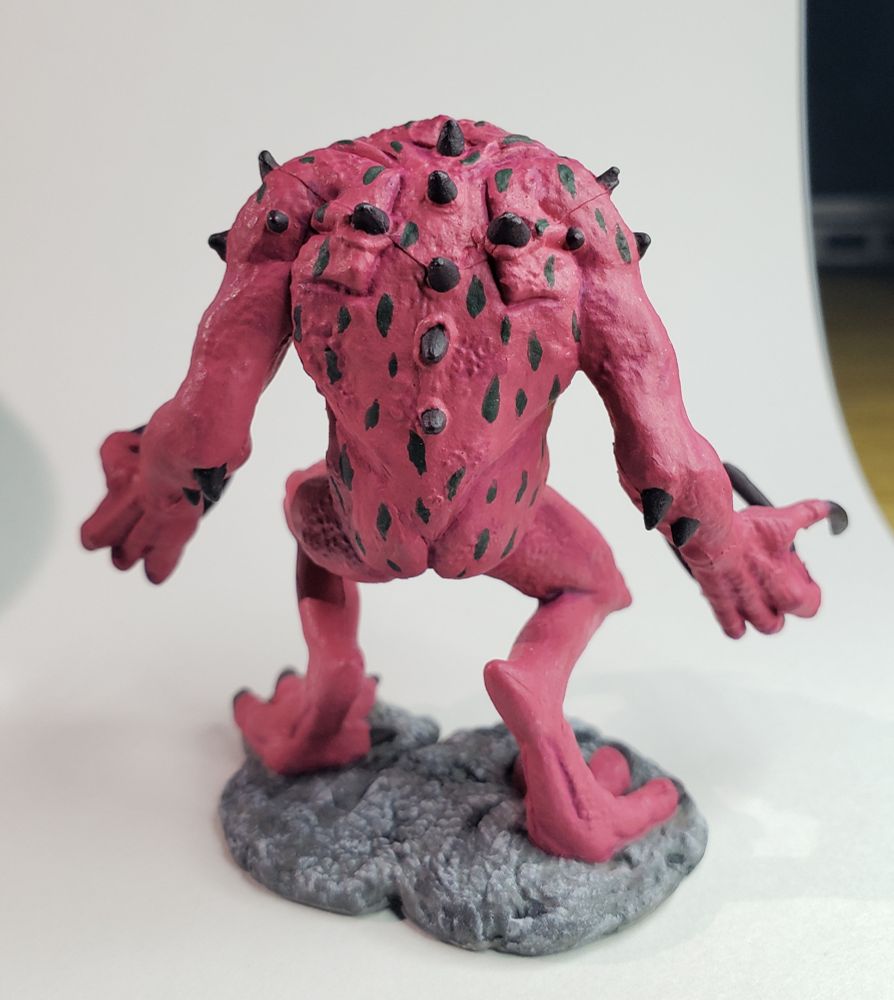 The back of the Red Slaad miniature. His back and elbows are adorned with dark spikes, and dark green markings cover his entire back. 