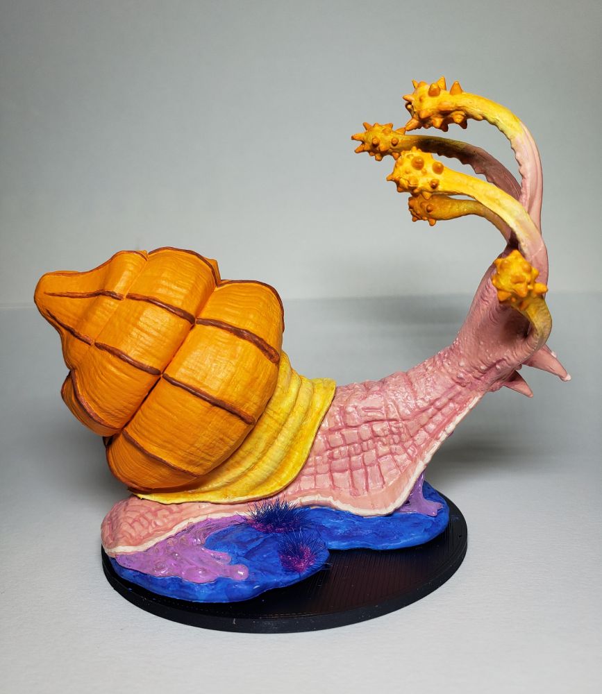 A side view of the snail. The view shows off the bulbous shape and size of the shell, as well as the bumpy texture of of the snail's body. Beside the snail are two tufts of blue grass, and behind it trails a short curved path of pink slime. 
