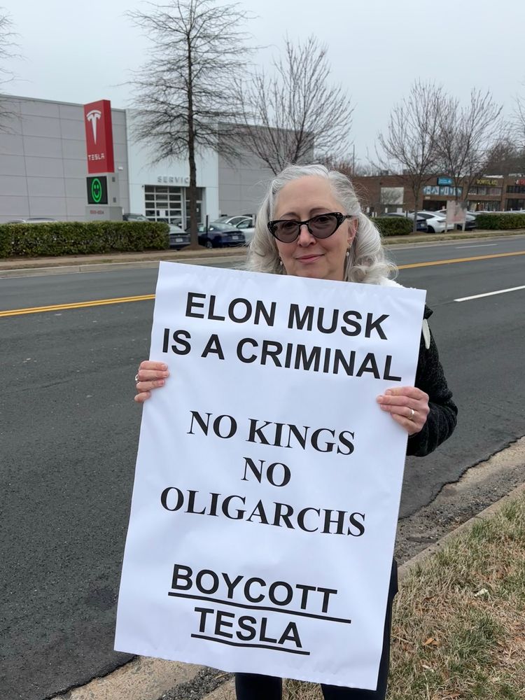 Holding a sign that says “Elon Musk is a criminal - No Kings -No Oligarchs - boycott Tesla - across from the Tesla dealership. 