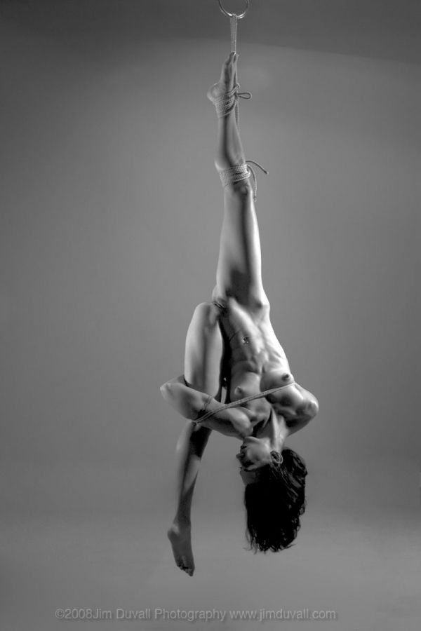 nude woman in yoga pose suspended upside down