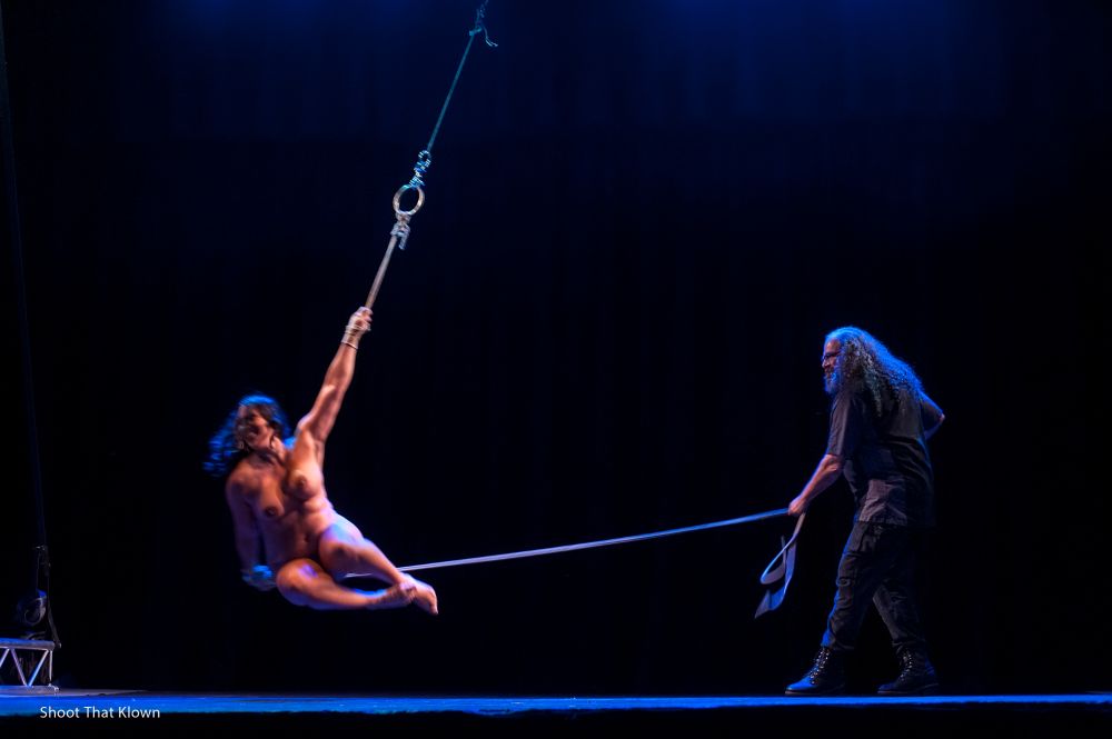 A nude woman swinging on a rope, being swing by a long haired man