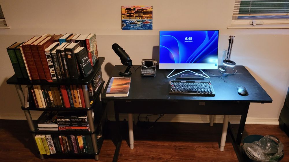 My writing center, including a typewriter-style keyboard, my bookcase, and a painting done by a former group- home resident.