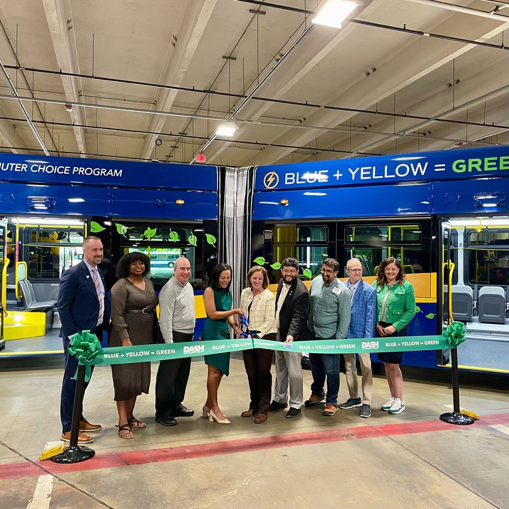 A photo depicting a group of people about to cut a ribbon in front of a new articulated bus
