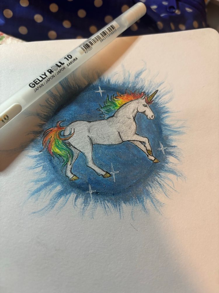 A sketchbook page with small drawing of a unicorn with rainbow mane and tail and a Gelly Roll gel pen. 