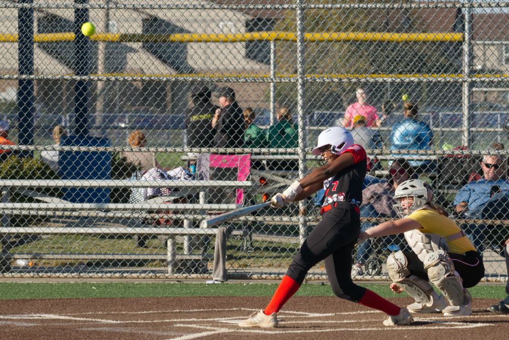 My daughter hitting a softball. Her arms are fully extended and she has an expression on her face that shows great effort. The ball is sailing away, almost out of frame. 