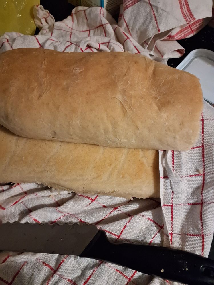 Kaksi tuoretta itse leivottua leipää valkoisen punaruudullisen kankaan päällä.