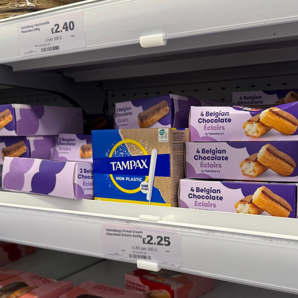 A box of Tampax tampons sitting in the fridge section of Sainsbury’s next to boxes of four chocolate eclairs.