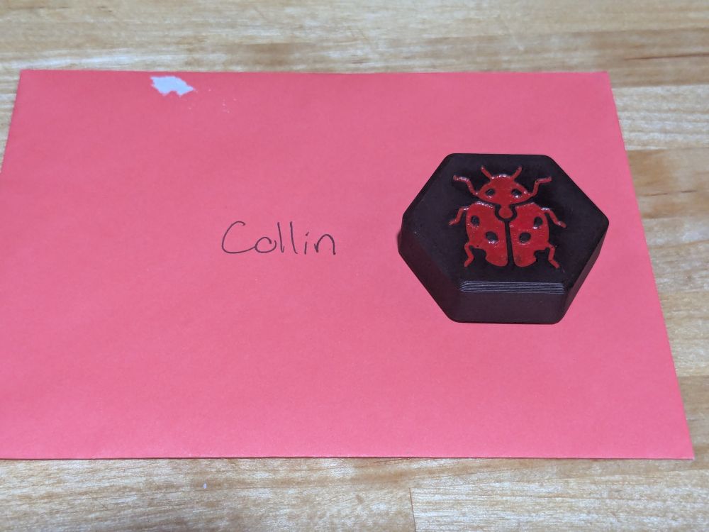Ladybug piece from the boardgame Hive on top of an envelope addressed to Collin