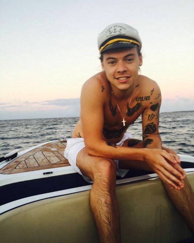 harry styles on a boat wearing a sailor’s (?) hat smiling at the camera 