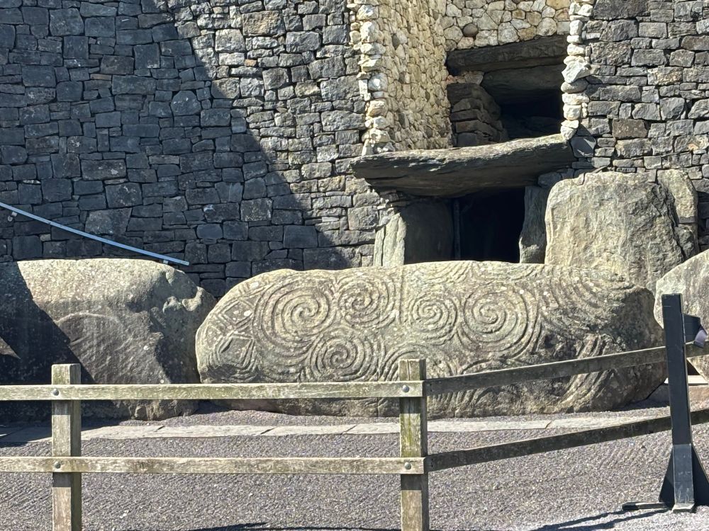 The entrance to the Newgrange monument featuring huge sandstone boulders decorated with hand carved spirals surrounded by a wooden fence
