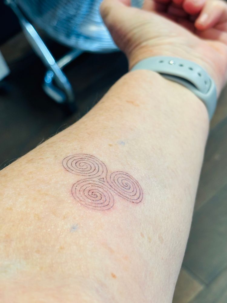 A tattoo on my left forearm of a triskele or triple spiral representing the connectedness of things and continuity. These symbols feature in the monuments at Bru na Boinne in Ireland 
My 2 daughters got the same one 
