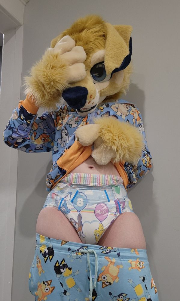 A woman in a golden retrieber fursuit lifts her Bluey sweater to reveal a soggy ABU tiny tails diaper under a pair of Bluey pajama pants