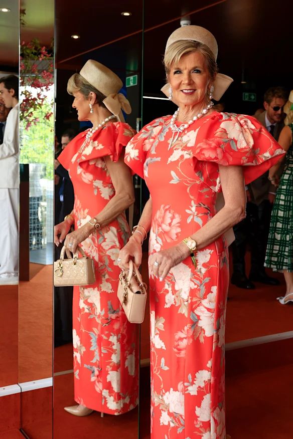 A woman in a bright orange dress with a beige handbag and pillbox hat 