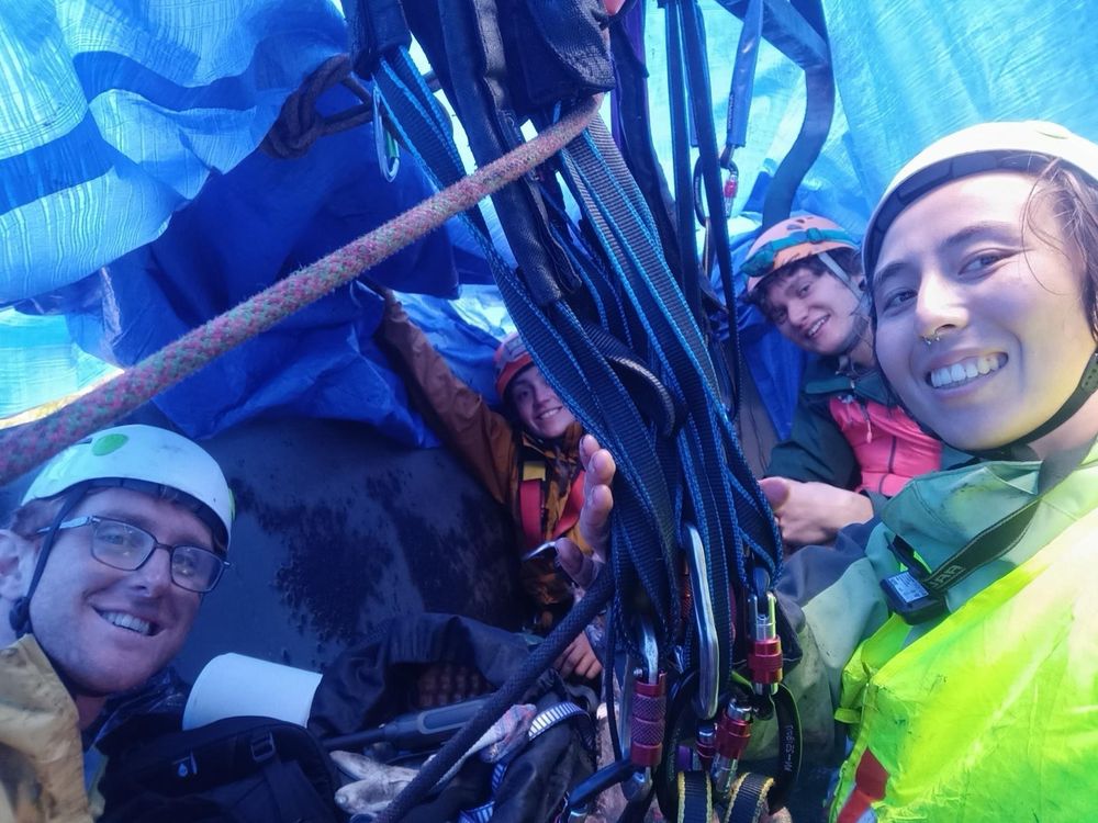 Four smiling people wearing hard hats and harnesses sit inside a coal car covered with a blue tarpaulin
