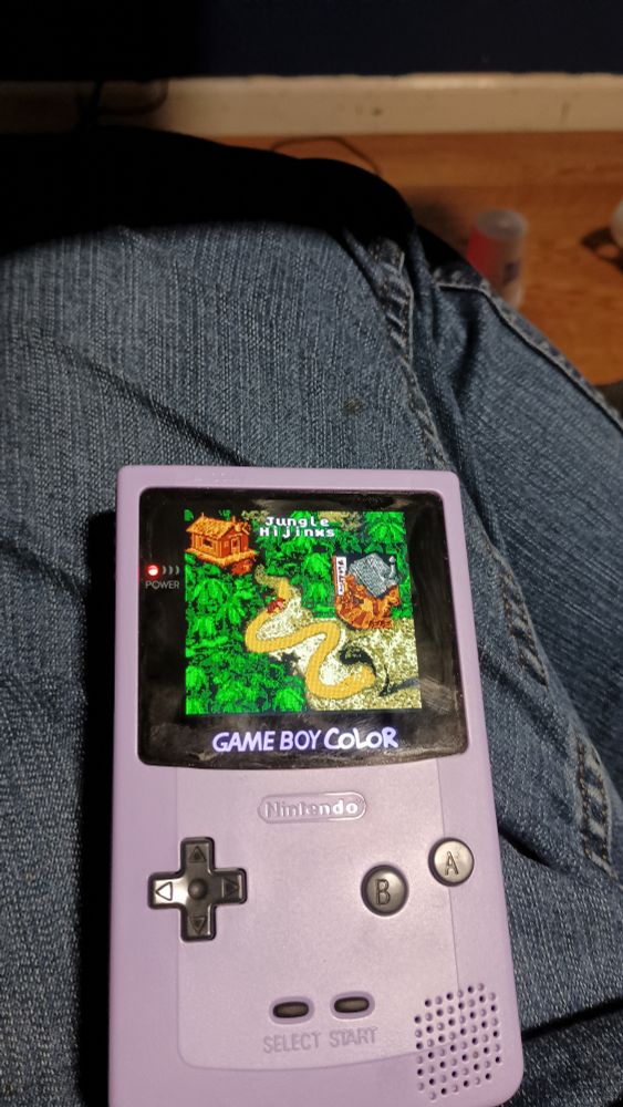 A purple game boy color displaying the game Donkey Kong Country.  A pixelated monkey appears on an overworks screen. 