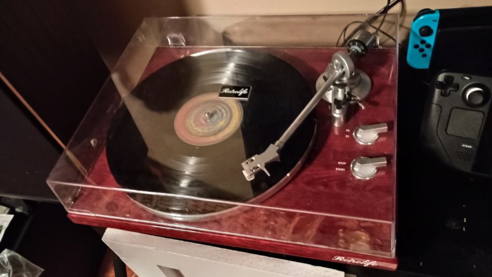 A vinyl record spinning next to a Nintendo switch and a steam deck