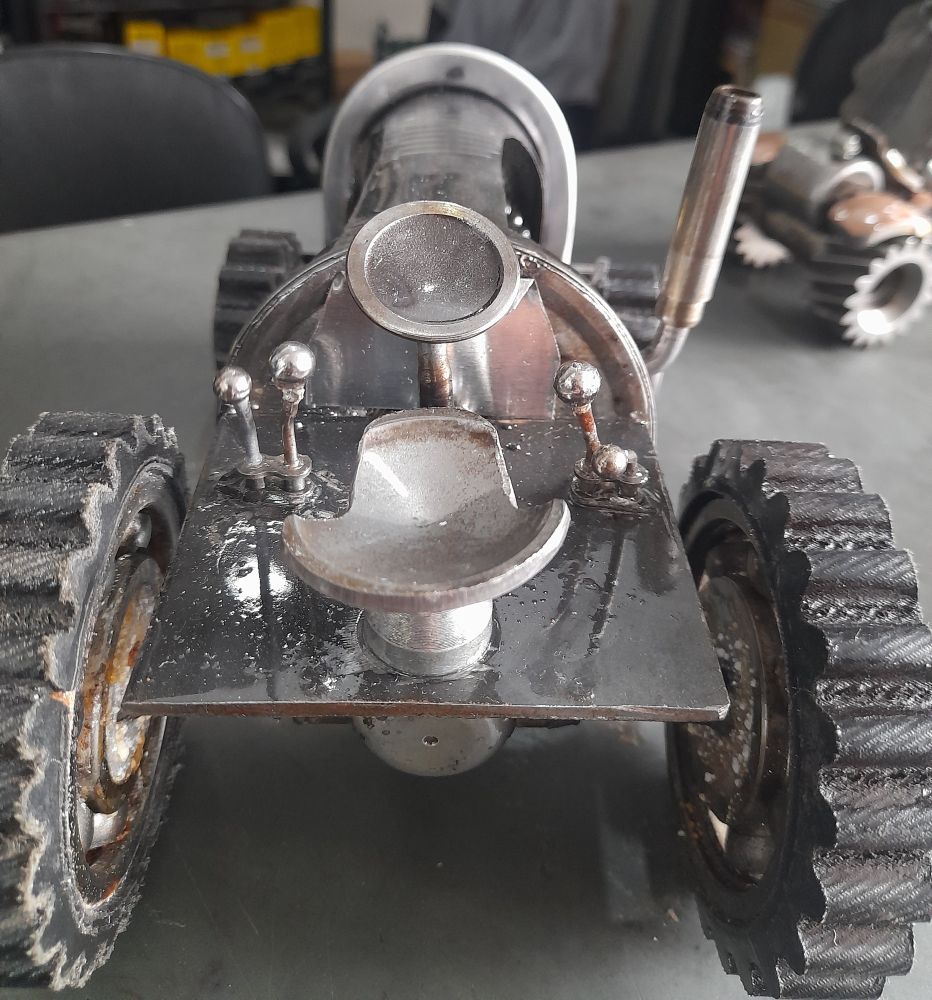 Trator de sucata vista traseira
Um banco com um volante e uma alavanca do lado direito e duas alavancas do lado esquerdo.