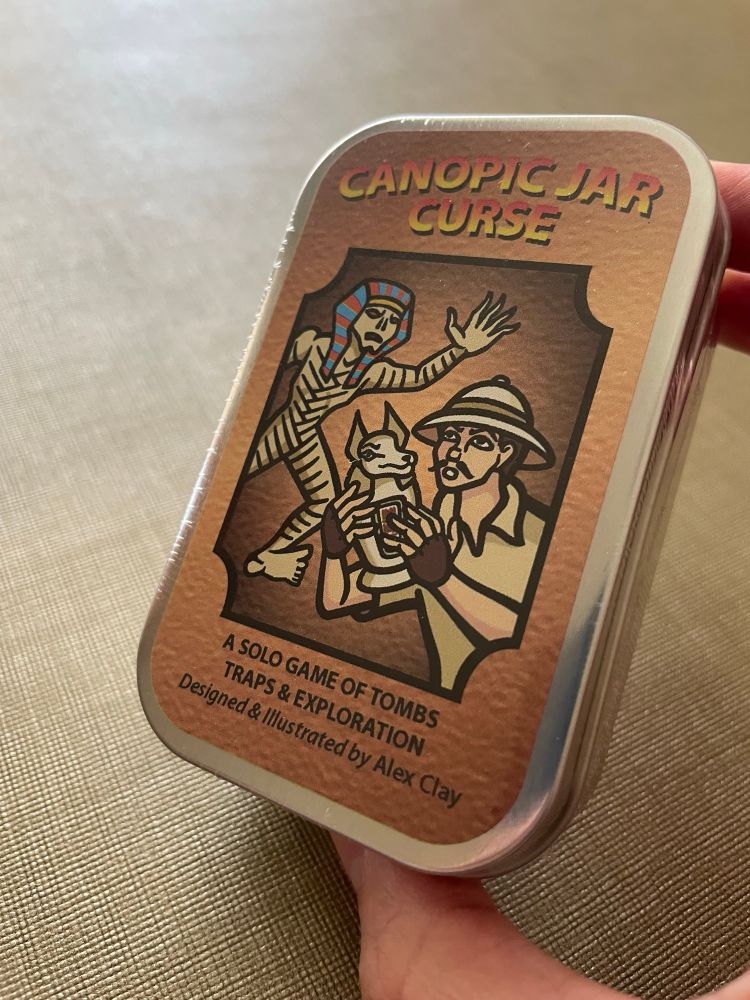 Mint tin game Canopic Jar Curse. The cover art shows an Egyptian mummy chasing an archeologist holding a canopic jar.