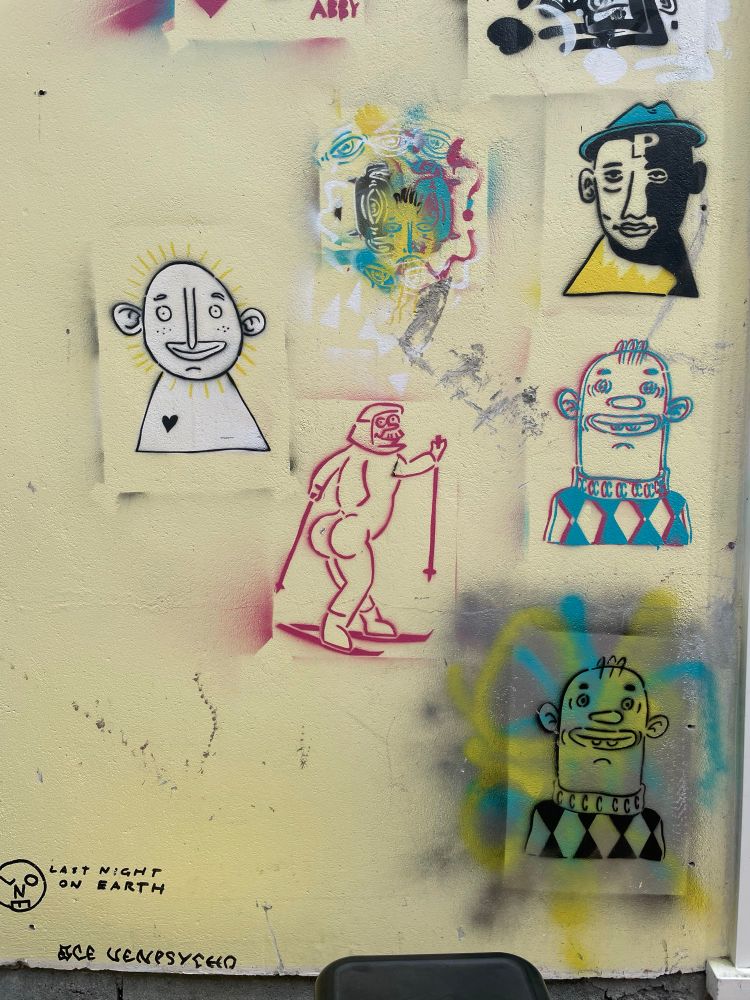 A wall decorated with colourful spray-painted stencils cartoon portraits. One resembles Ned Flanders in a red skin-tight ski suit from a Simpsons episode.