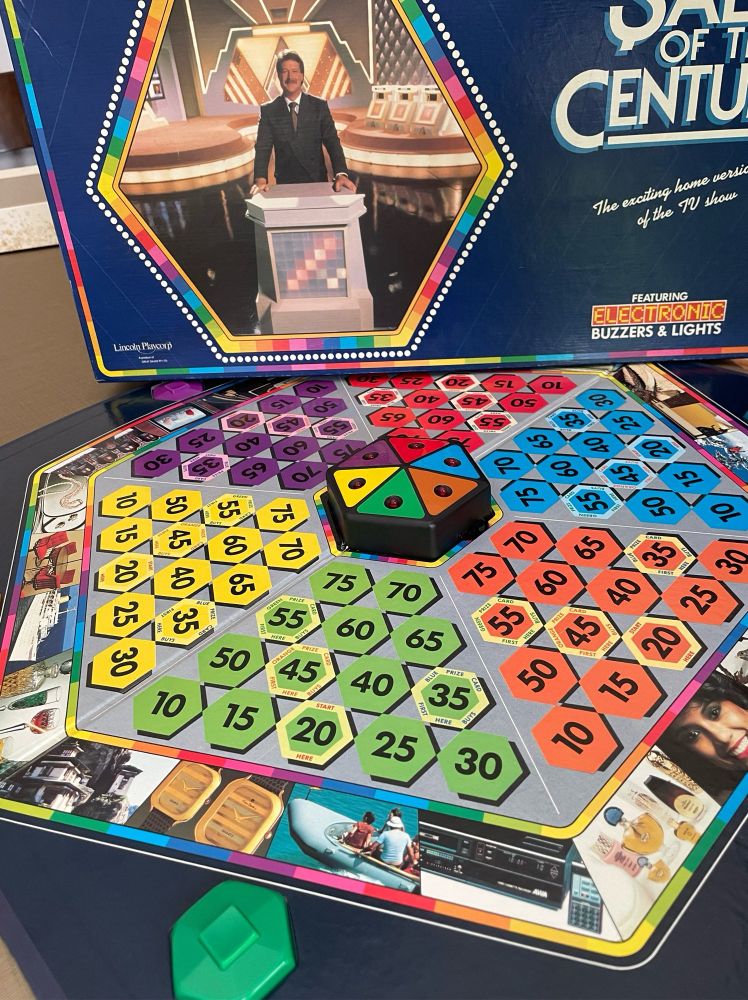 “Sale of The Century” board game based on the TV quiz show from the 80’s(?). Colorful hexagon prize money stepping stones are surrounded by photos of quiz show prizes from the era.