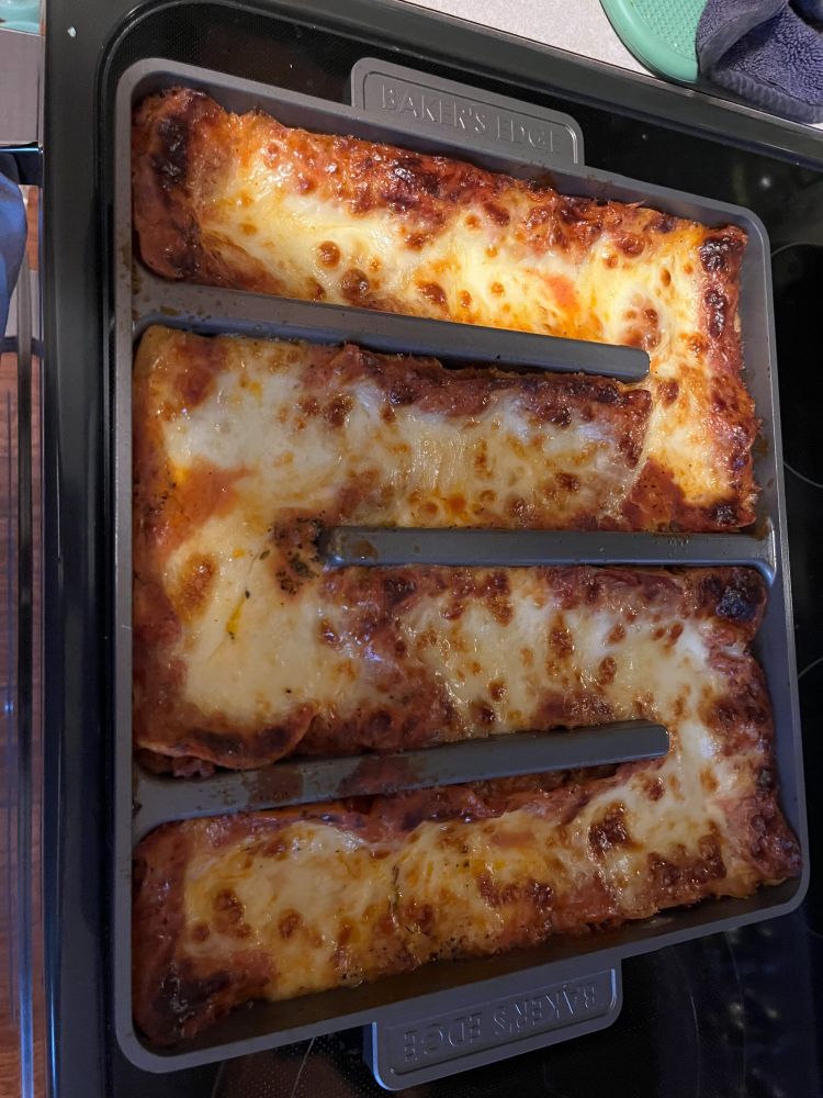 A baked lasagna in a Baker's Edge pan on a stovetop.