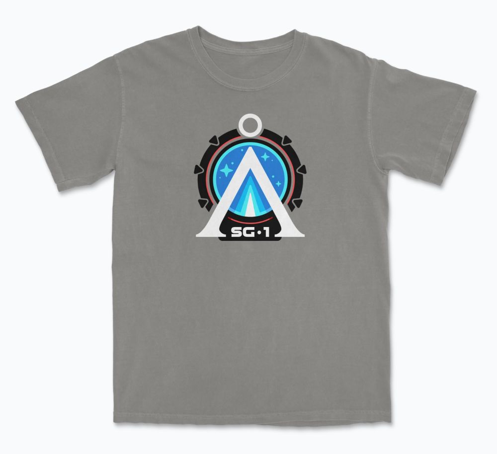 Graphic T-shirt showing the Earth Chevron in white against a black Stargate with the letters SG-1 at the bottom. Shown on a tan/grey shirt.