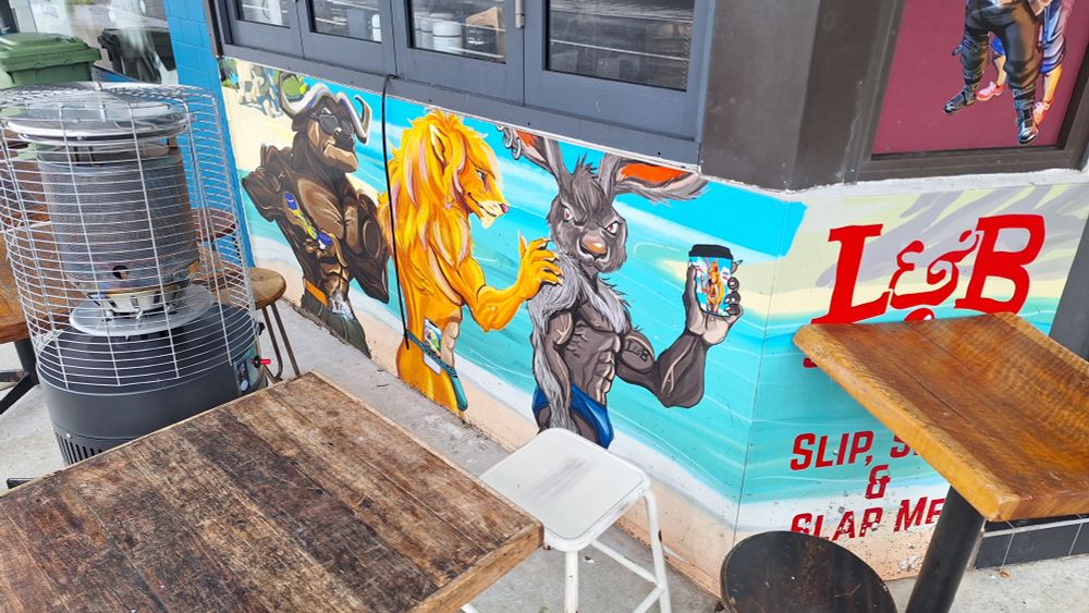 An inexplicable mural on the wall of a Sydney café depicting three ripped animals. The text, partially obscured, reads "Slip, Slop & Slap Me".