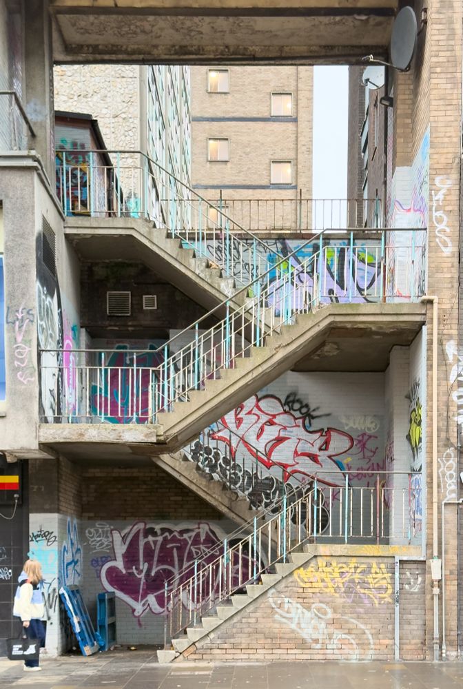 Open concrete stairs between 3 storey buildings. There is colourful graffiti
