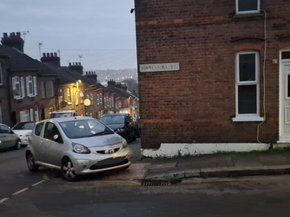 A silver car parked across the corner of a junction, covering the tactile paving.