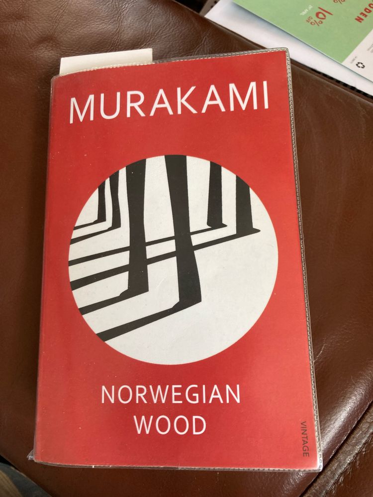 A red book cover with a white circle in the centre, filled with black tree trunks in a wood, with dramatic black shadows. Text reads Murakami, Norwegian Wood.