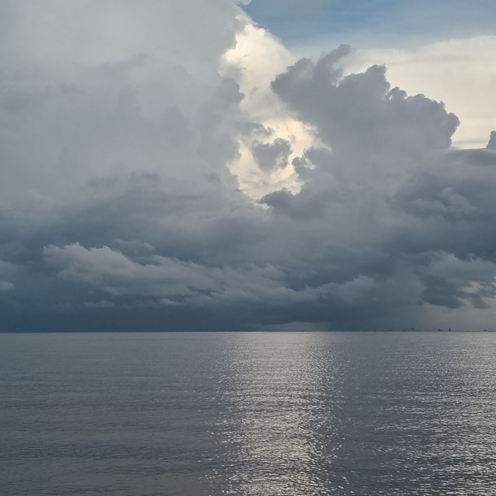 Stormy grey cloudy sky covers the calm sea. There's a shining path over the sea where the last of the sun is trying to get through.
