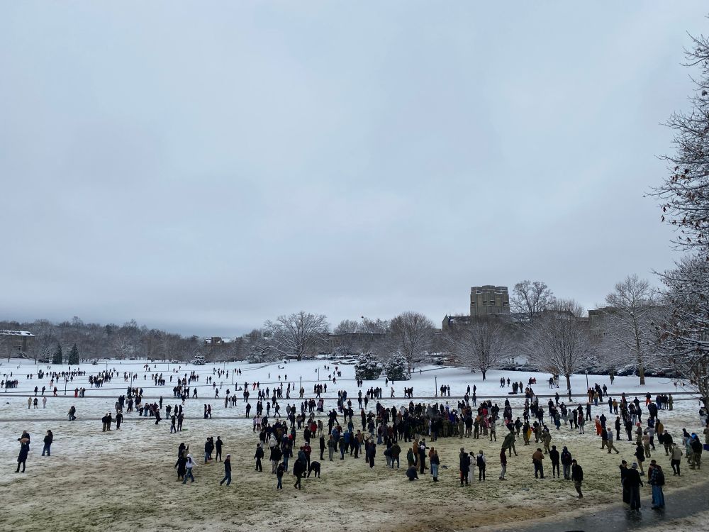Tech students are seen throwing snowballs on the Drillfield with campus buildings in the background 