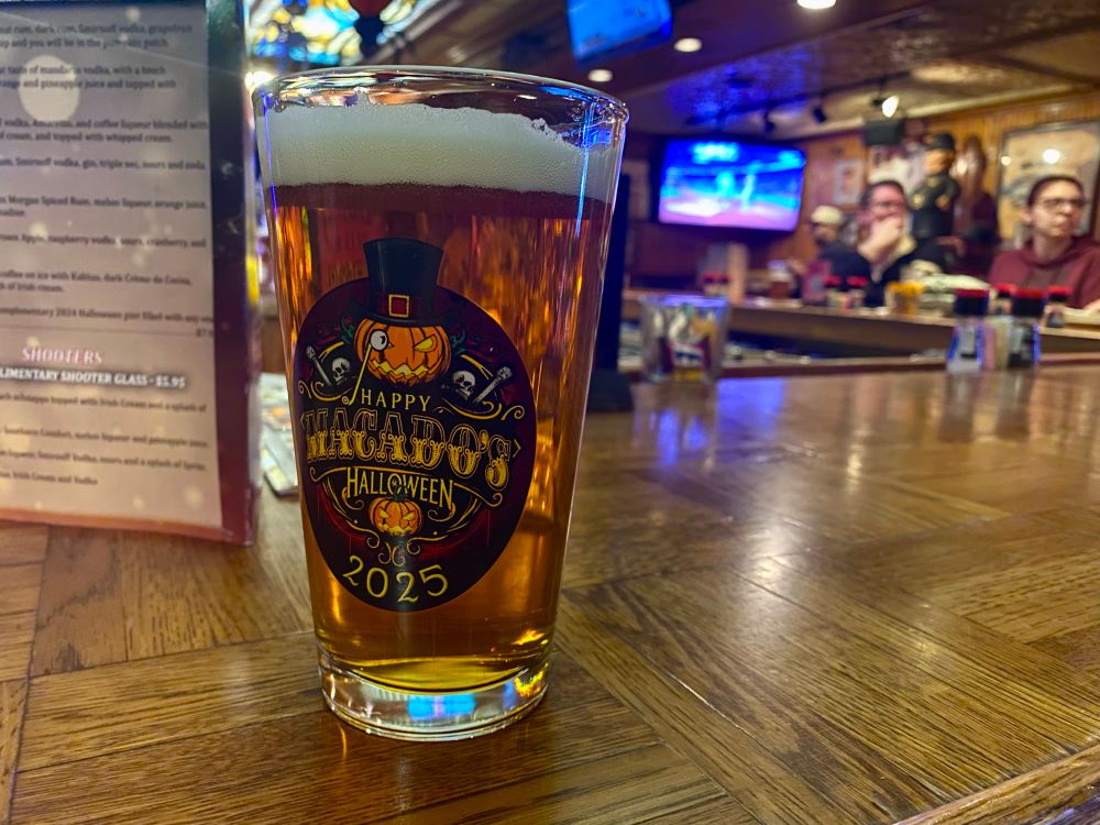 A pumpkin ale is depicted in the annual Macado’s steal-a-pint glass with bar patrons and a tv seen in the background 