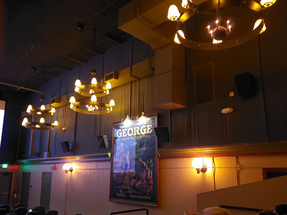 Side wall of the movie theater with chandeliers and an antique magician poster