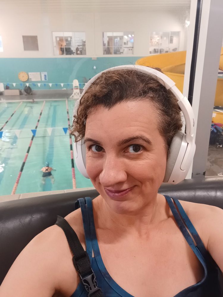 Shawna, a.k.a. forty-something white lady with curly brown hair, big brown eyes, and chunky white headphones. She is sitting in front of a window overlooking an indoor pool at a YMCA.