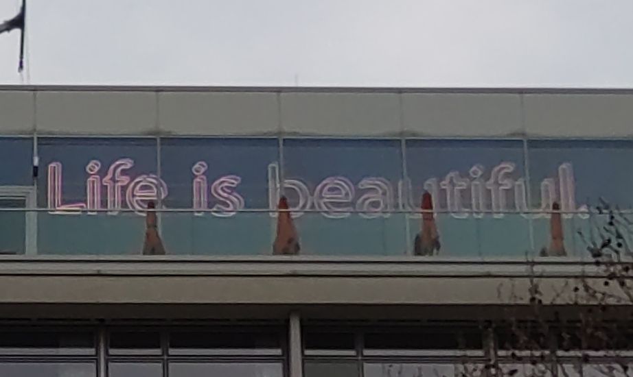 "Life is beautiful." als Schriftzug neon pink beleuchteter Schriftzug an einer Hotelfassade.