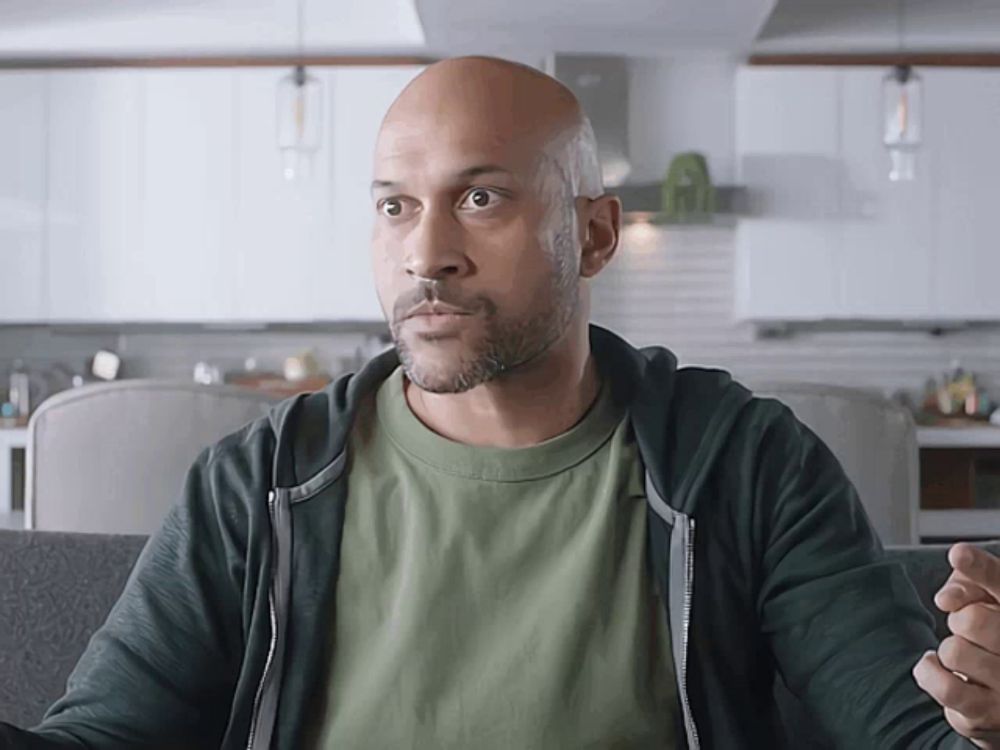 a bald man in a green shirt and black hoodie