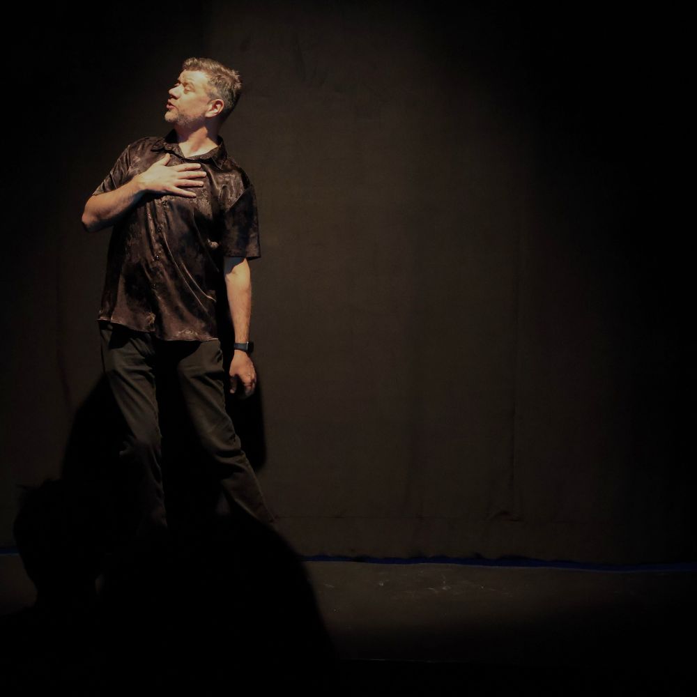 Stephen stands onstage in the spot light at an improv show. 