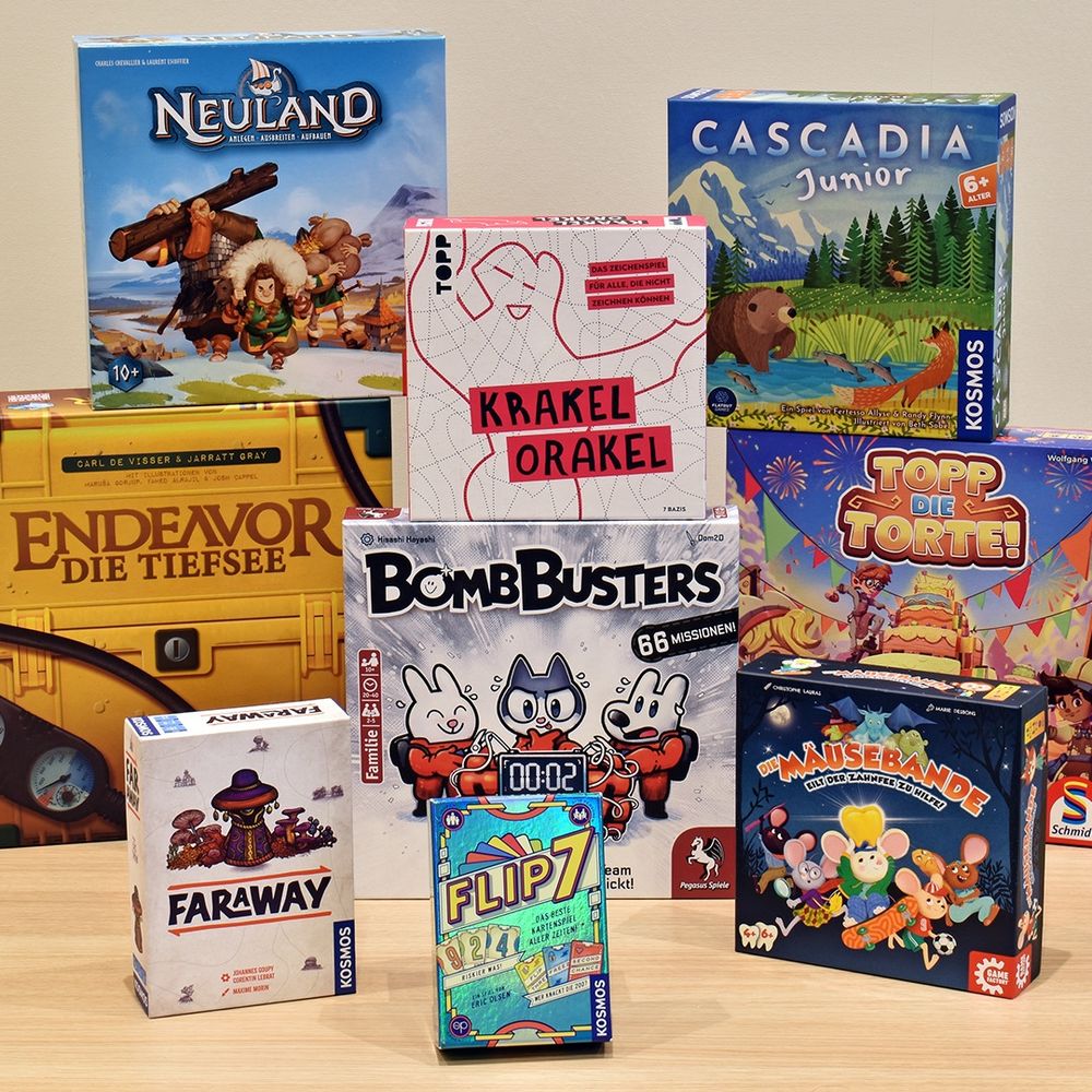 Alle Nominierten Spiele zusammen auf einem Tisch.
Vorne Flip 7, Faraway und Die Mäusebande, dahinter Bomb Busters, darauf steht Krakel Orakel. Rechts daneben Topp die Torte auf dem Cascadia Junior steht und links daneben Endeavor die Tiefsee auf dem Neuland steht.
